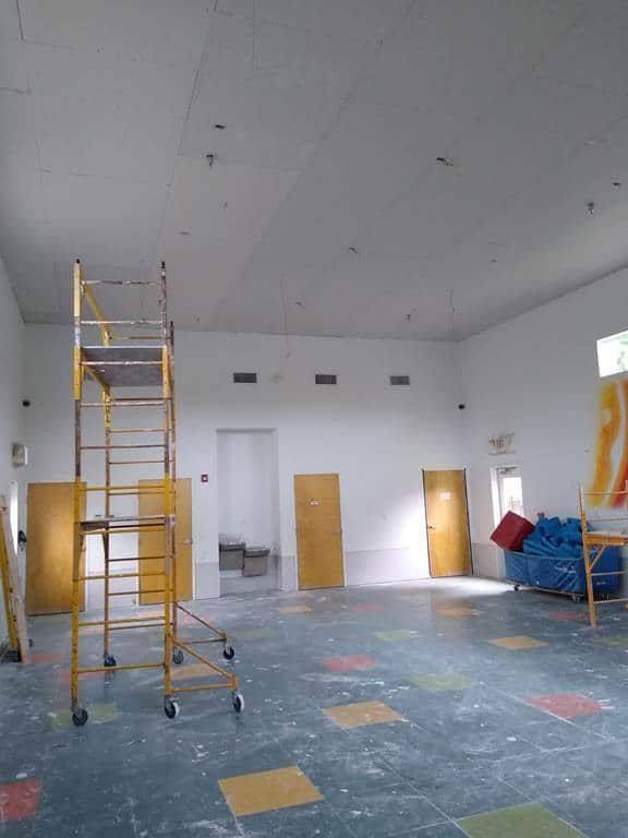 The same gymnasium mid-recovery, with the new ceiling installed and scaffolding still in place over the stained original floor