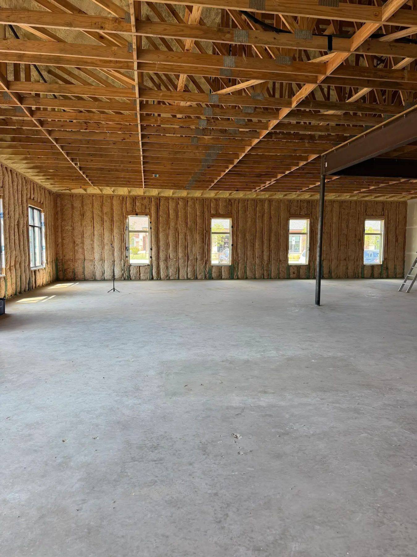 The empty 3,000 sq ft shell space for Aleaf Insurance in Frisco, TX before construction, with a bare slab and open timber trusses