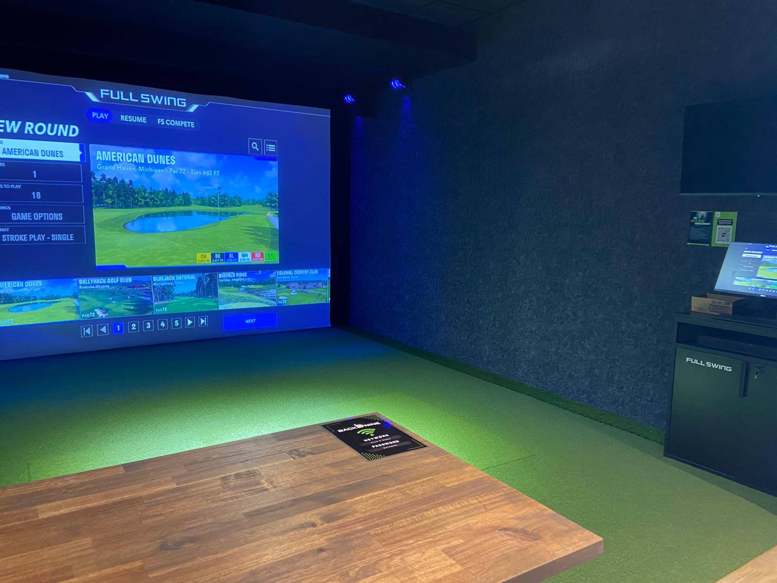 Finished golf simulator bay with a full-wall projection screen and turf hitting floor at The Back Nine Golf in Denton, TX