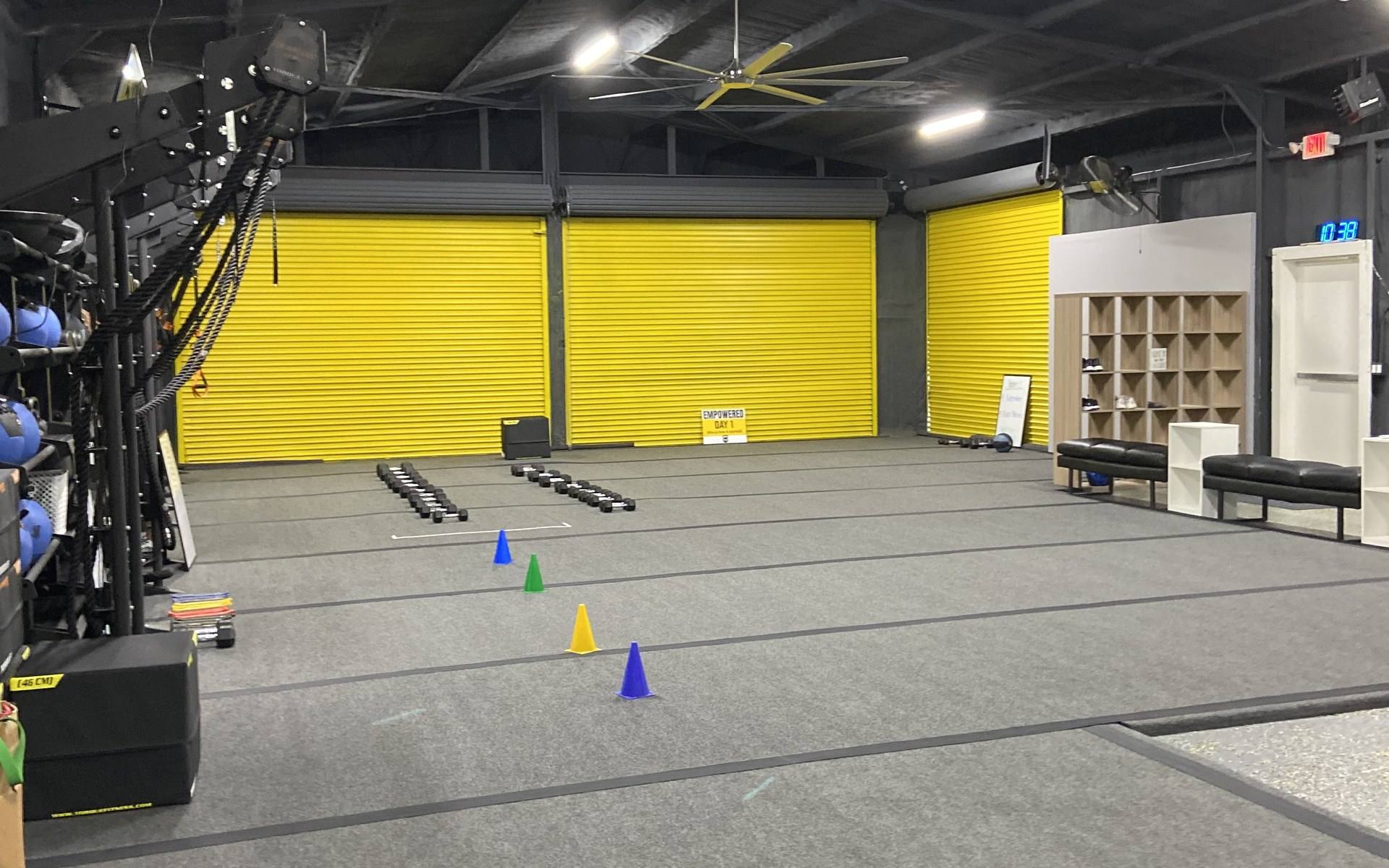 The finished training floor at Empower 35 Fitness in Frisco, TX, with the roll-up doors repainted yellow and rubber flooring throughout