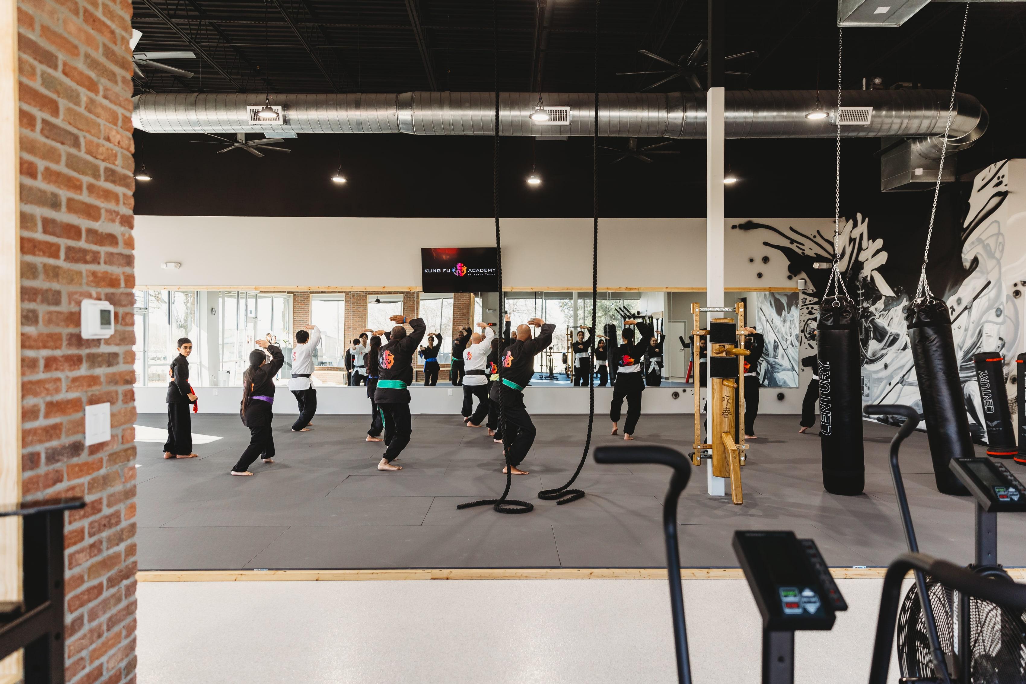 Martial arts class training on the finished mat at Kung Fu Academy of North Texas, with an exposed brick column, full-height mirrored wall, and open ceiling, remodeled by NorthStar Commercial Interiors