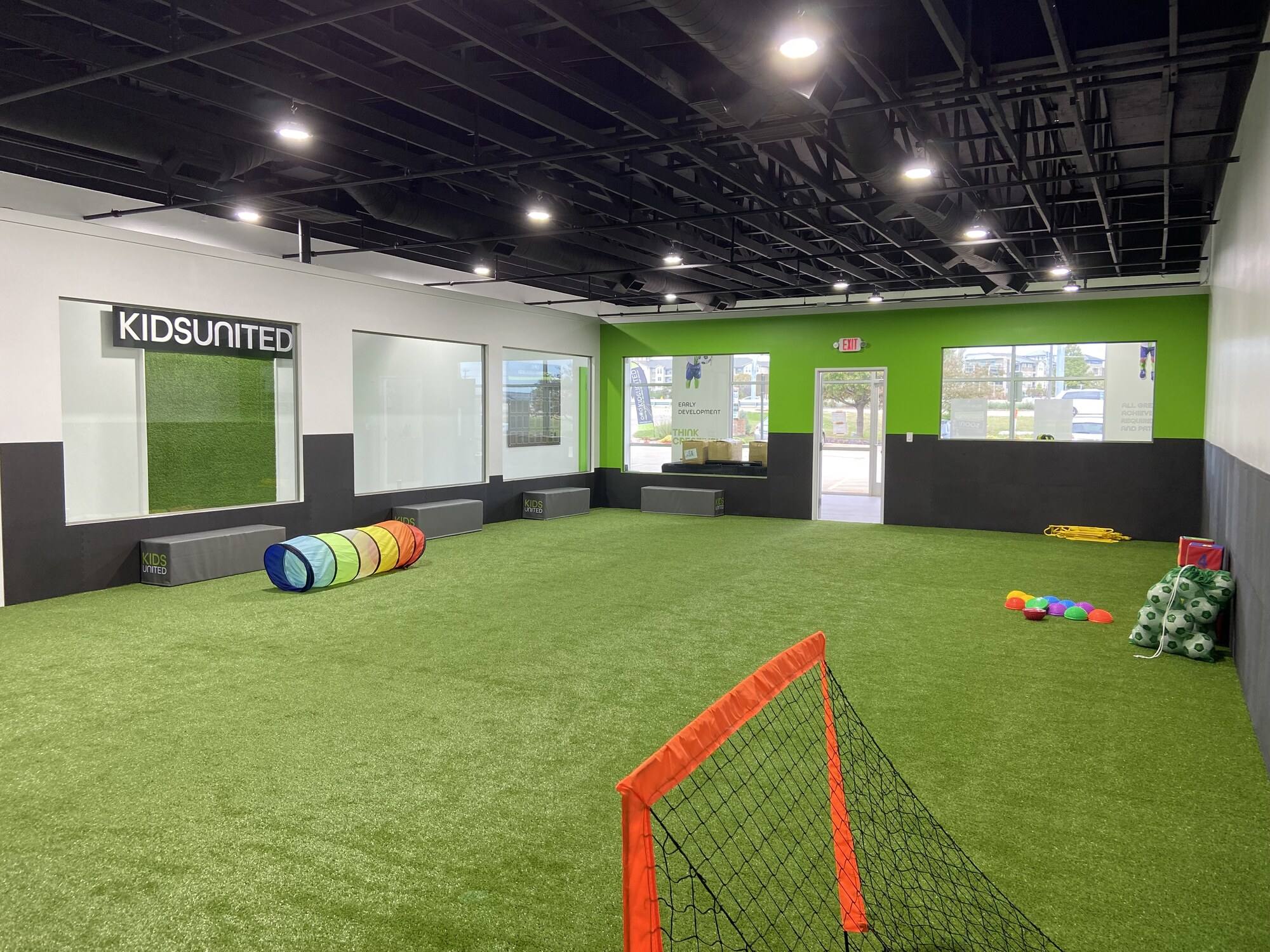 The finished Kids United turf training floor in Plano, TX, with goals, padded walls and the branded window bay