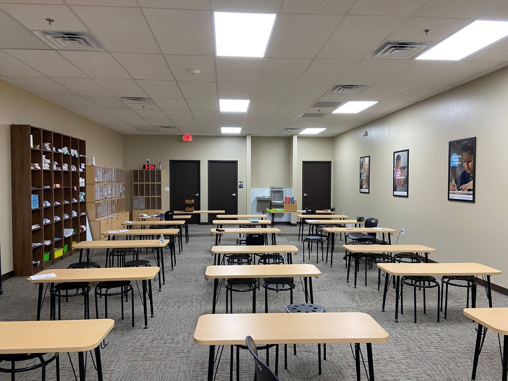 The finished classroom at the Kumon Learning Center in Melissa, TX, with rows of study tables and stools under a grid ceiling and the student material shelves along the left wall