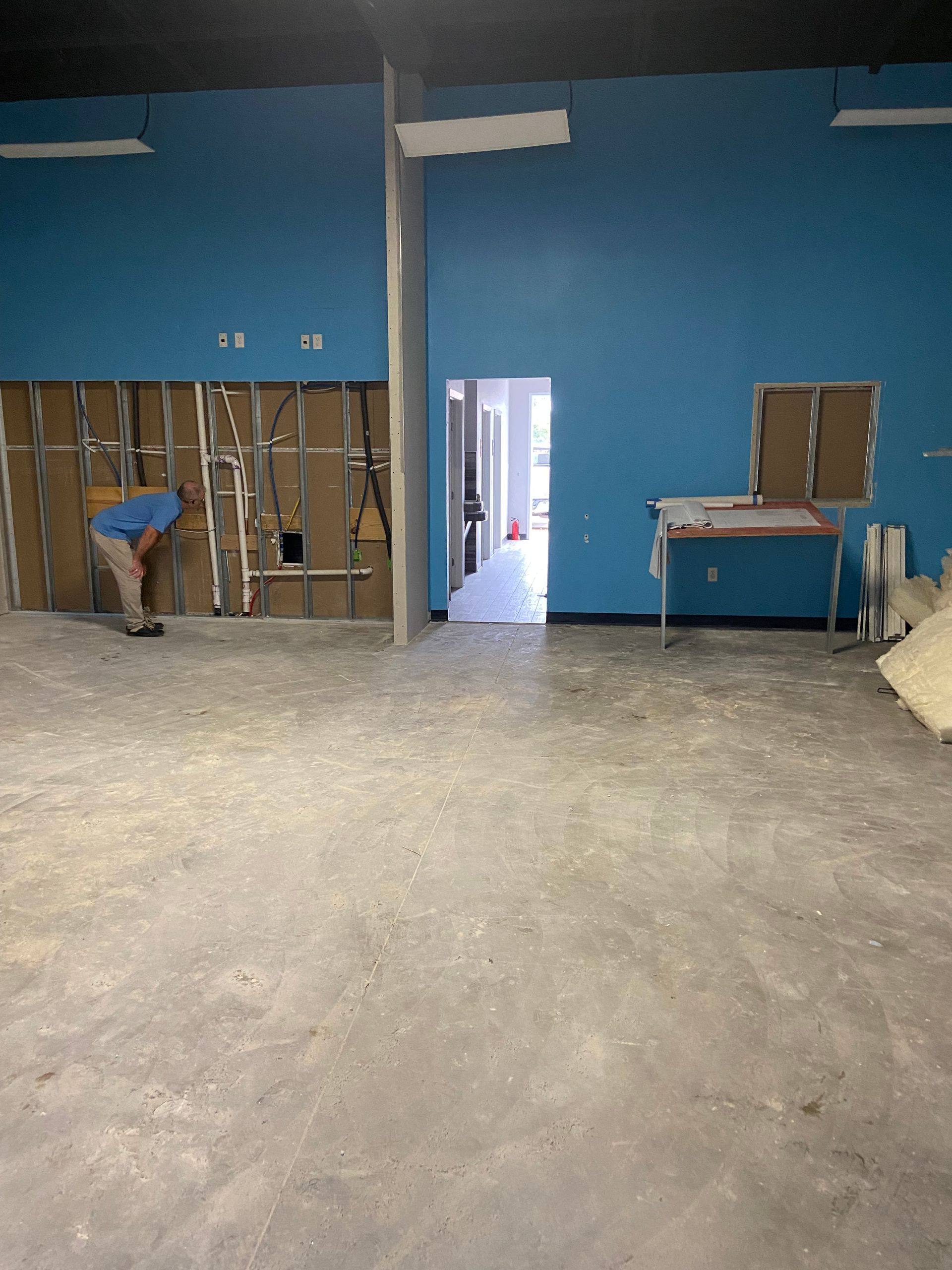 Progress: the main room stripped back to bare concrete during the Augment Wellness remodel in Frisco, TX, with new plumbing and electrical run in the opened wall